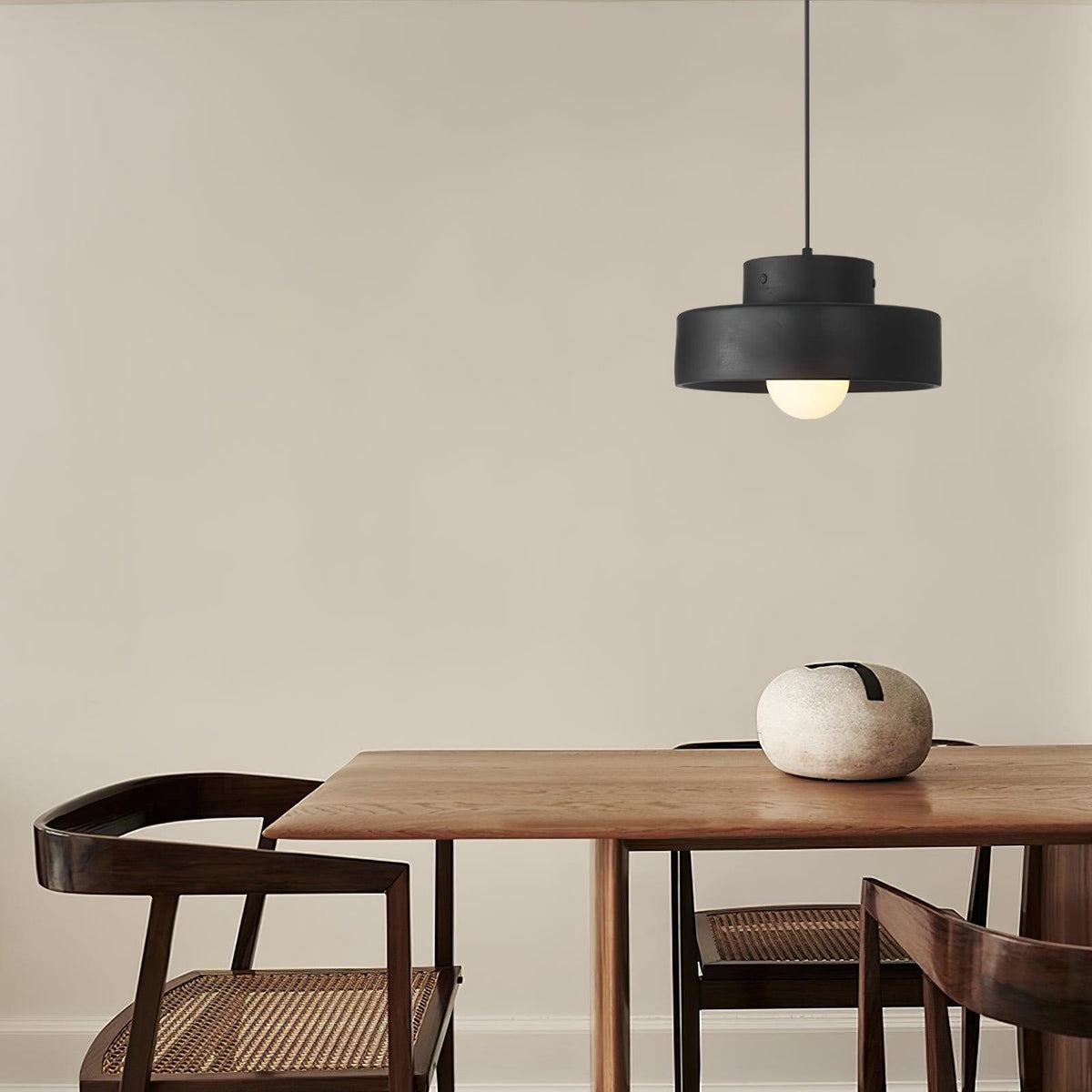 This black Clérachic pendant hangs high in the corner of a dining room above a walnut table with a pale stone bowl and cane-seated chairs.