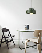 Green Clérachic pendant on a white wall above a round marble-topped table, a folding chair and a moulded plywood chair.