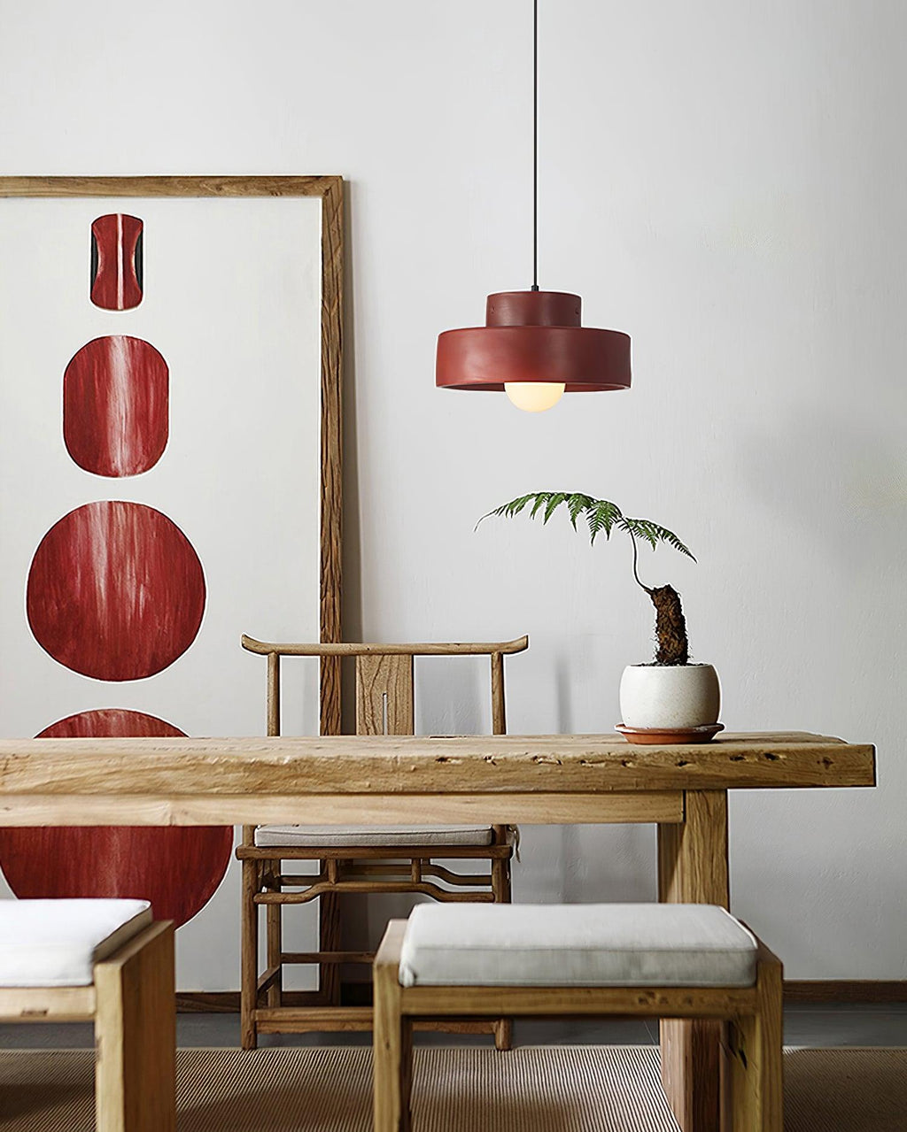 Red Clérachic pendant on a white wall beside a framed red artwork, above a carved wooden table with a fern in a white pot.