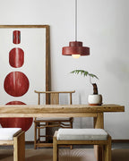 Red Clérachic pendant on a white wall beside a framed red artwork, above a carved wooden table with a fern in a white pot.