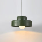 A green Clérachic pendant lit against a soft grey wall, with a pool of warm light on the surface below.