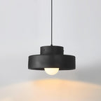 Black Clérachic pendant lit against a soft grey wall, its stepped shade and round bulb casting warm light below.