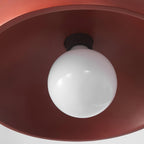 Looking up into the red shade of this Clérachic pendant, with the black bulb holder and a white globe bulb at the centre.