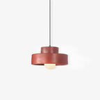 A red Clérachic pendant with a slightly uneven, matte resin finish, hanging on a black cord against a pale backdrop.