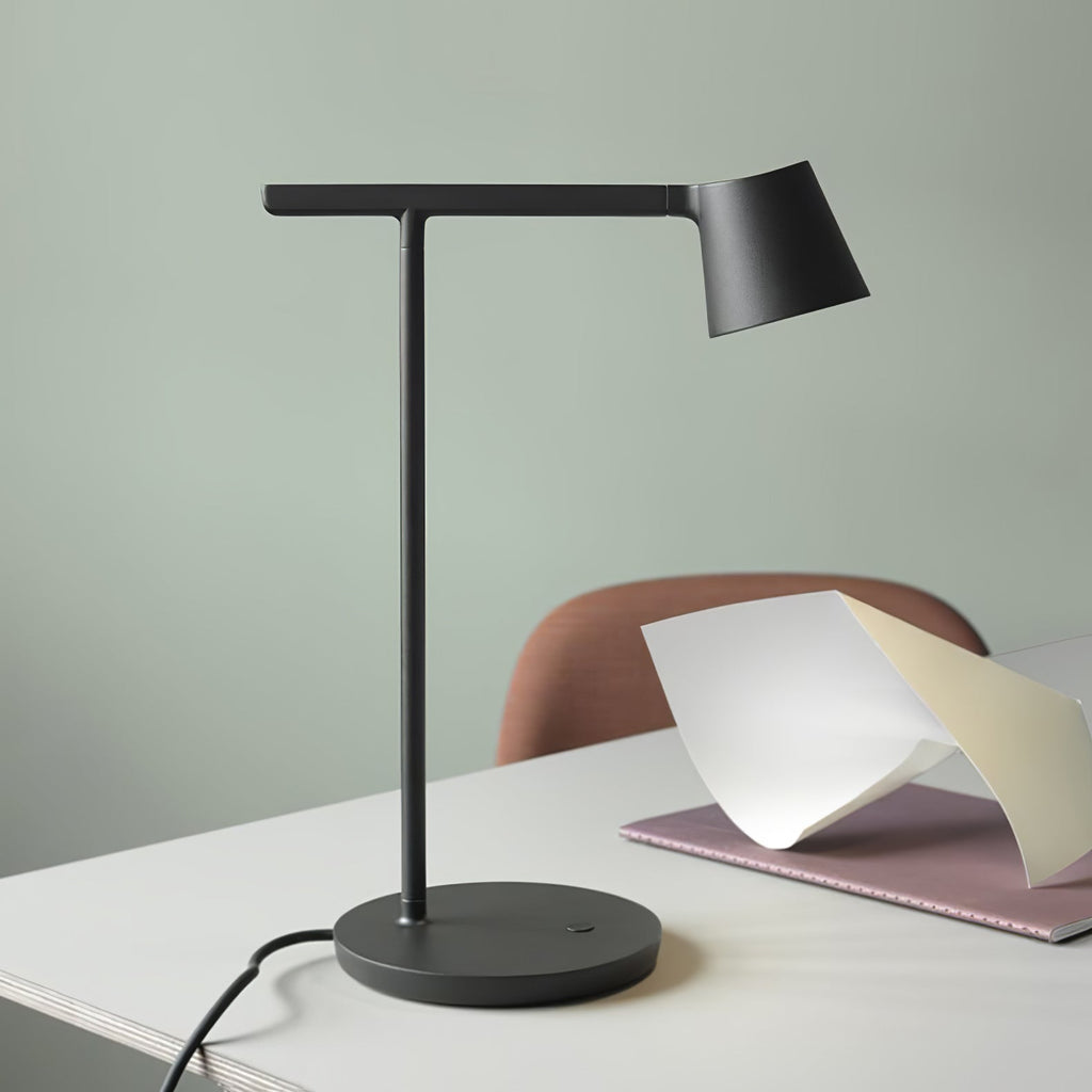 This Clérachic table lamp in black on a white desk against a sage-green wall, with a pink notebook and folded paper beside it.