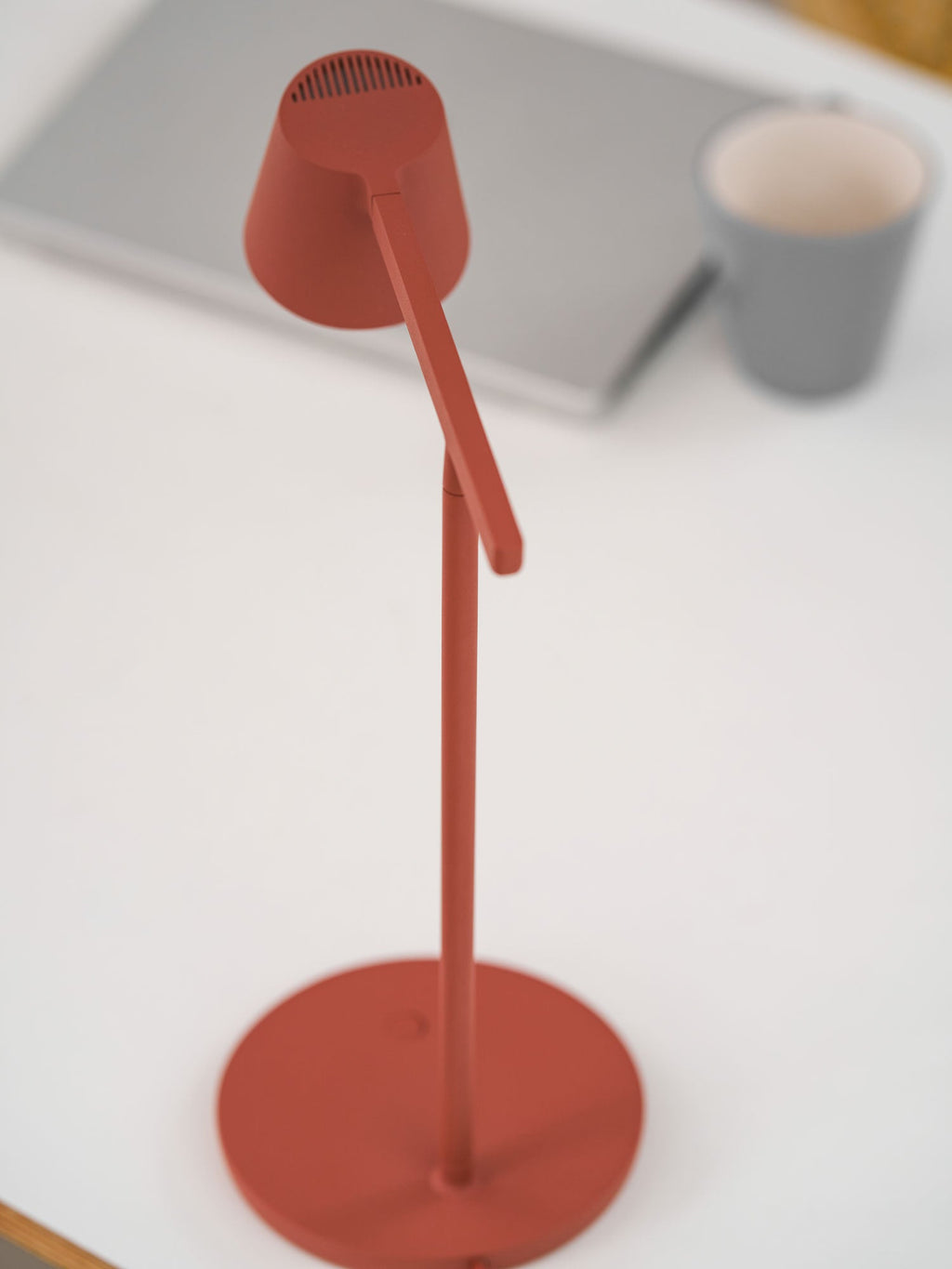 Close view of the red head and round base of this Clérachic table lamp, switched off, with a grey cup behind.