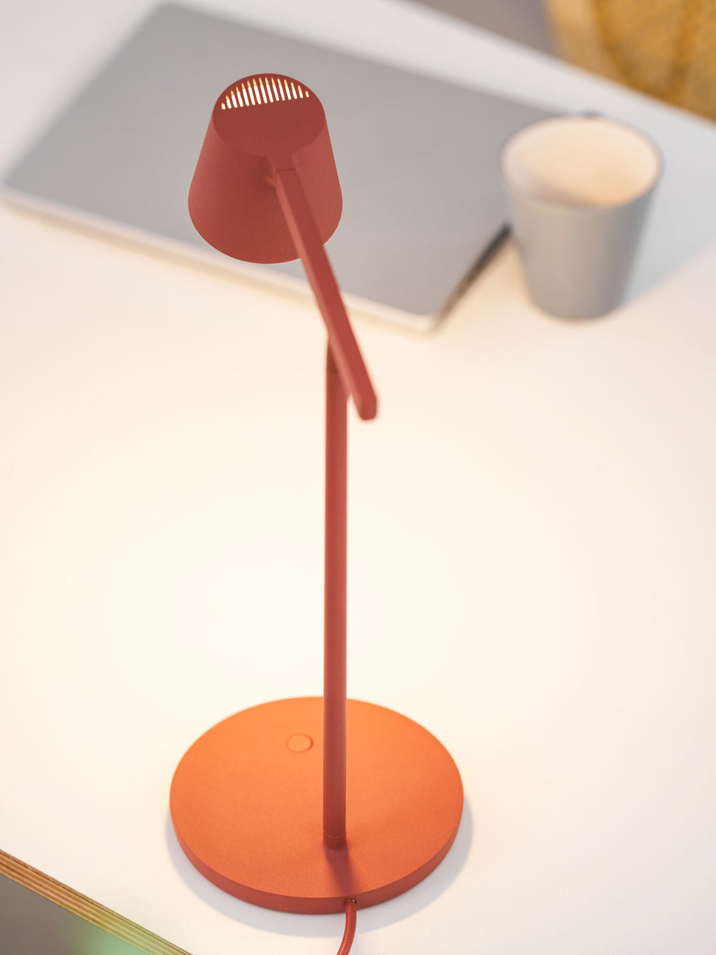 The same red Clérachic table lamp switched on, with a warm glow lighting the white desk and the head's vents.