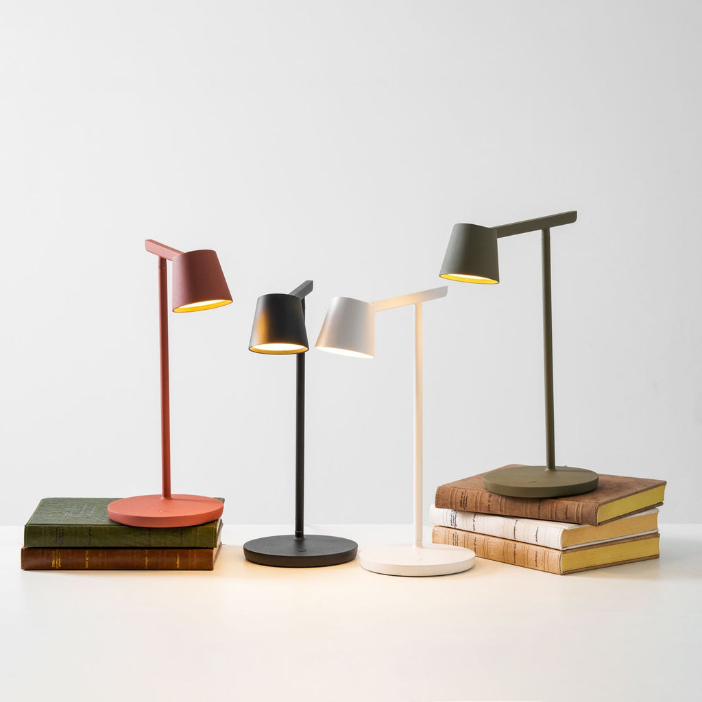 Four Clérachic table lamps on a white surface, two of them resting on stacks of old books, all with lit heads.