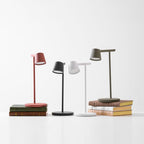 A group of four Clérachic table lamps on white, with the red and olive lamps on stacks of cloth-bound books.