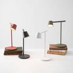Four Clérachic table lamps at different angles, with the red and olive ones standing on old books on a white surface.