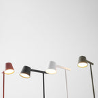 Low angle on four Clérachic table lamps in red, black, white and olive, with their heads lit against pale grey.