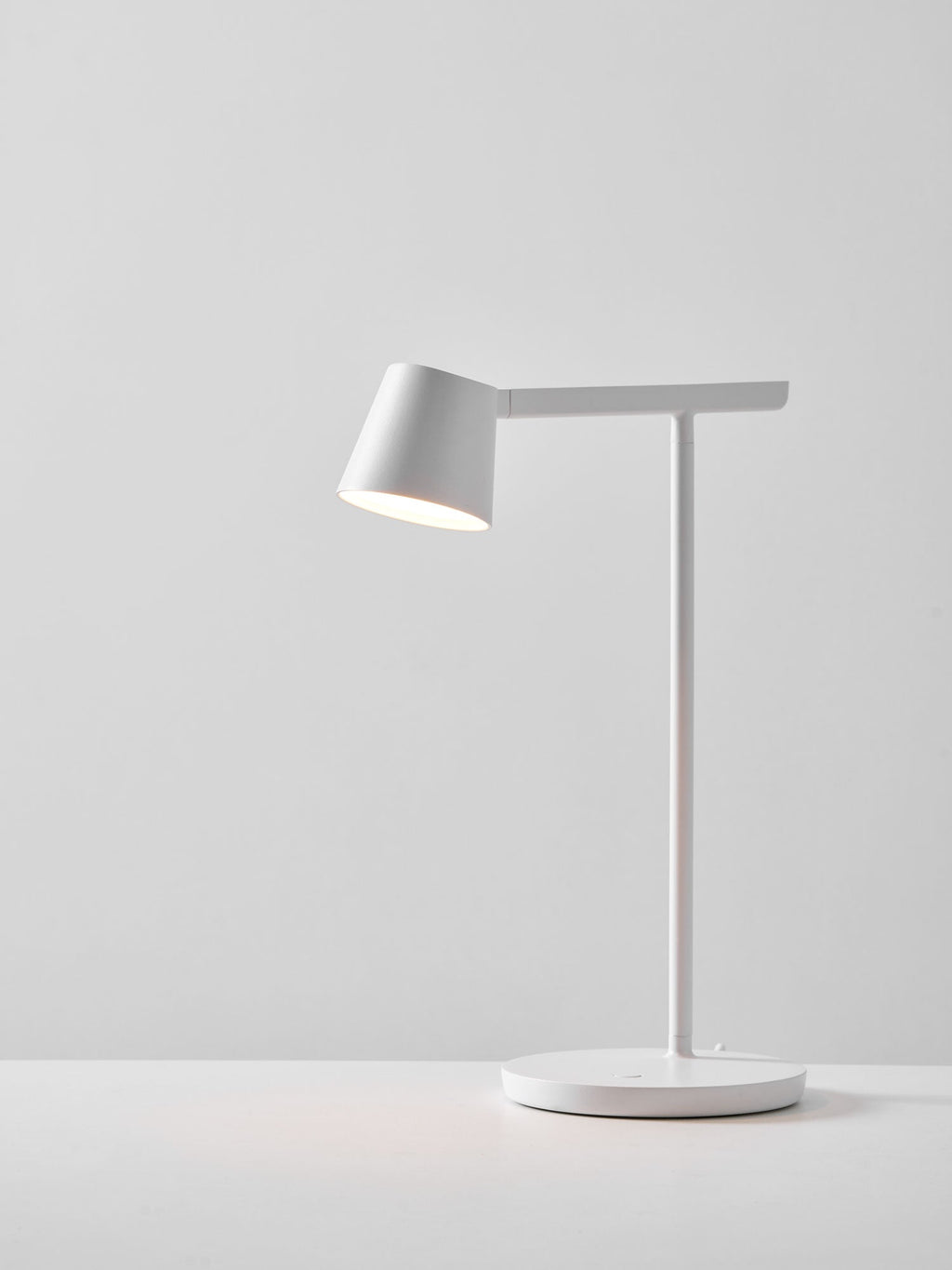 White Clérachic table lamp lit on a pale grey backdrop, with a soft pool of light on the surface beneath.