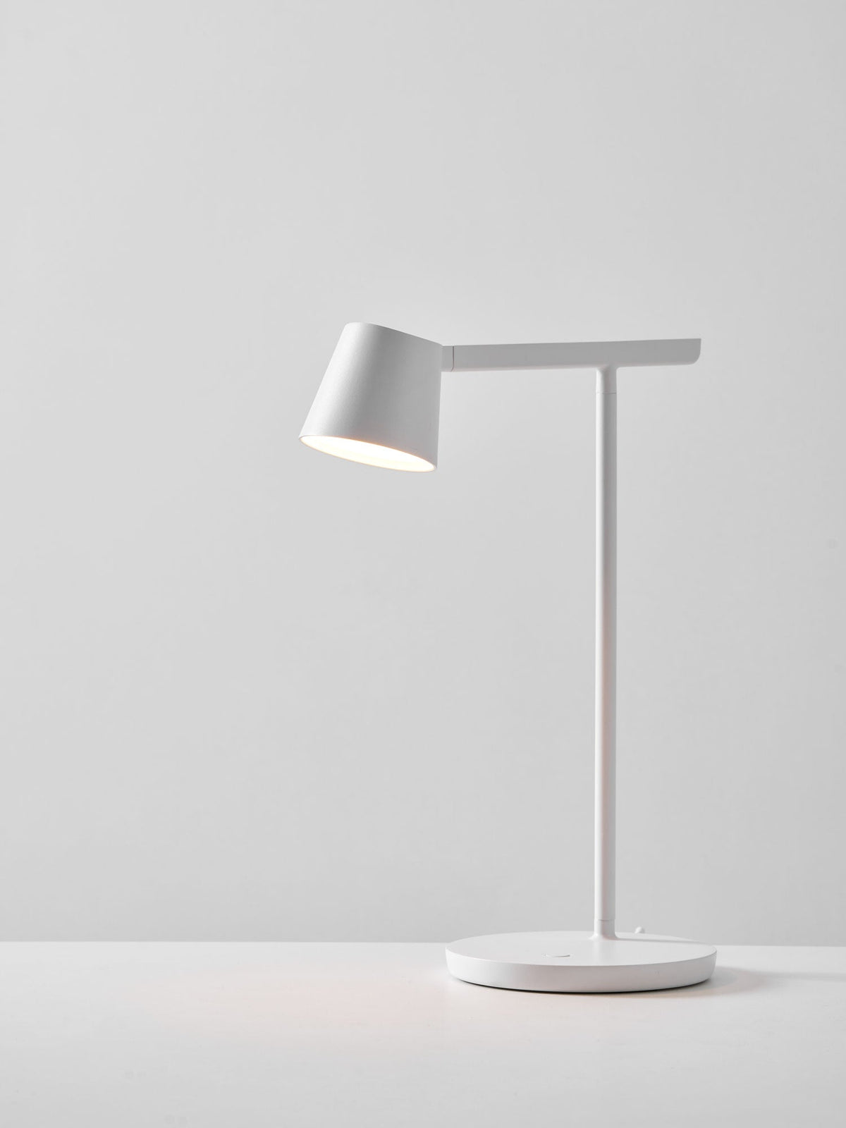 White Clérachic table lamp lit on a pale grey backdrop, with a soft pool of light on the surface beneath.