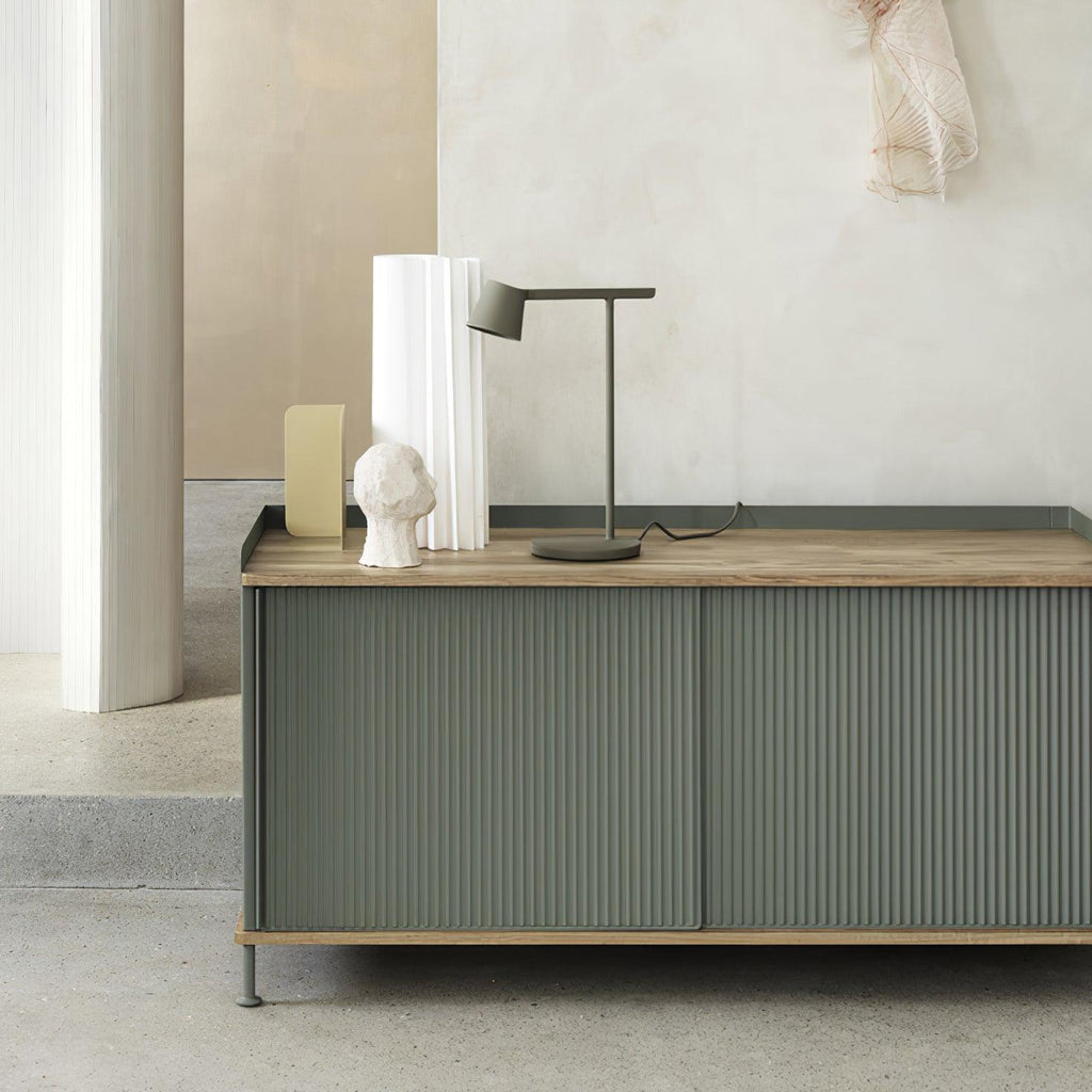 An olive Clérachic table lamp on a green sideboard with a wooden top, next to white vases and a small plaster head.