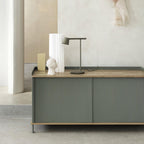 An olive Clérachic table lamp on a green sideboard with a wooden top, next to white vases and a small plaster head.