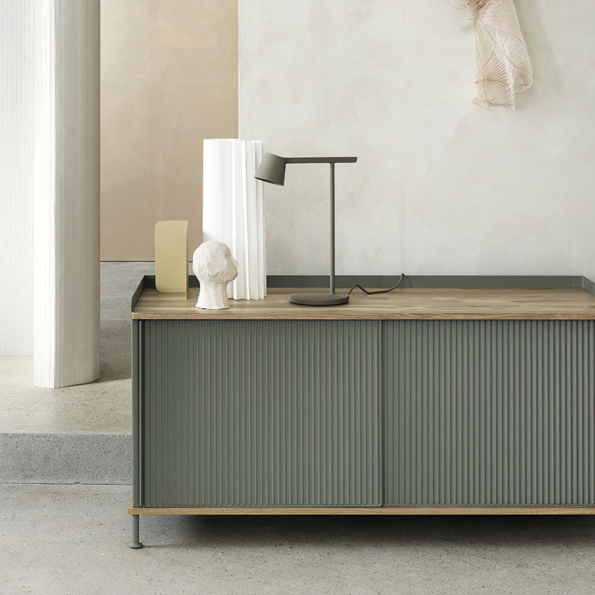 An olive Clérachic table lamp on a green sideboard with a wooden top, next to white vases and a small plaster head.