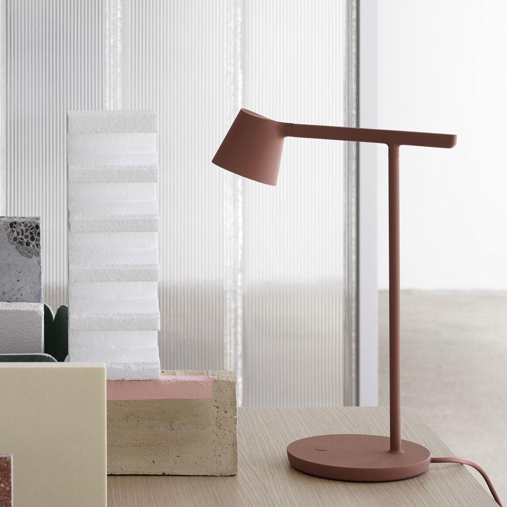 A rust-red Clérachic table lamp beside stacked white blocks, with a ribbed glass screen behind it.