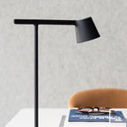Close view of the black head and slim arm of this Clérachic table lamp, with a blue book and glasses blurred behind.