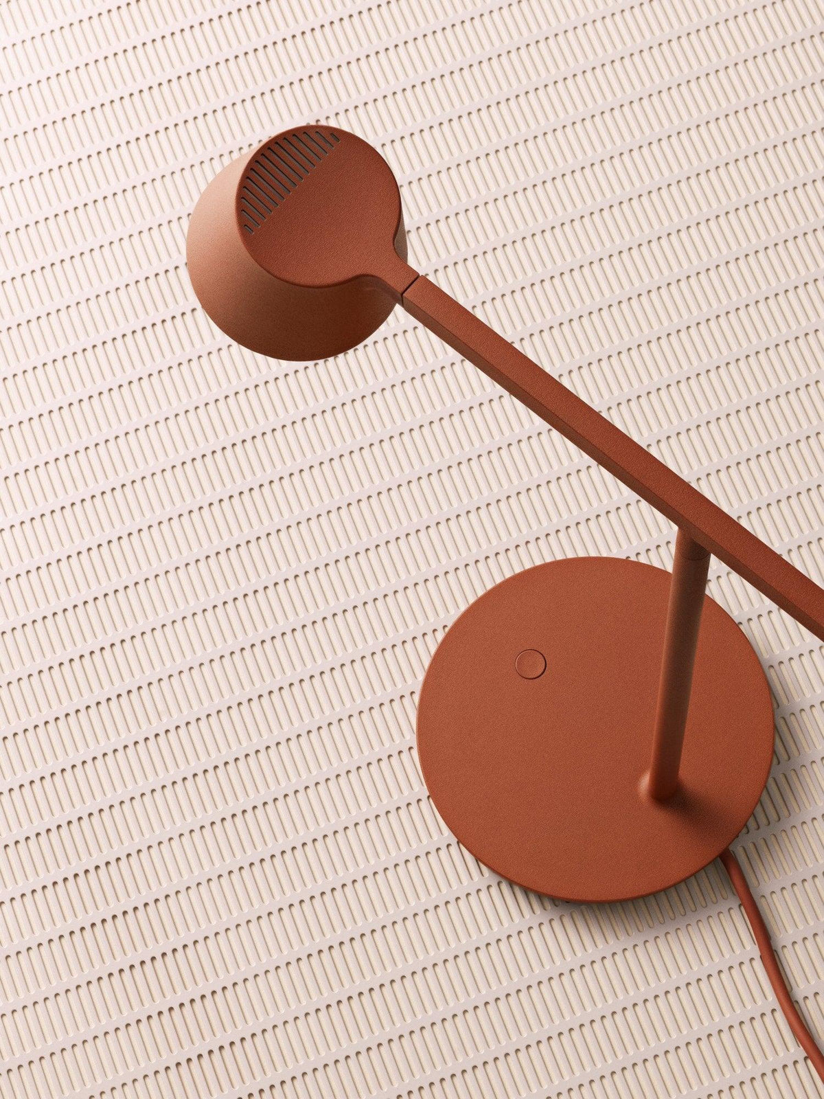 Overhead view of a rust-red Clérachic table lamp, showing the round head, thin arm and disc base on a pale tiled surface.