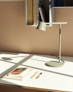 This Clérachic table lamp in olive with window light casting long shadows over a white desk, books and a pen.