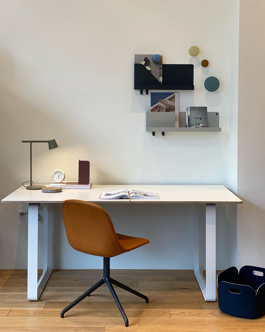 This Clérachic table lamp in olive at the end of a white desk with a tan chair and a wall shelf above.