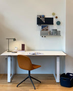 This Clérachic table lamp in olive at the end of a white desk with a tan chair and a wall shelf above.