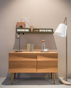 A small olive Clérachic table lamp on a green wall shelf above an oak sideboard, with a white floor lamp at the right.