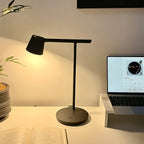 This Clérachic table lamp in black lit warmly on a desk, with a laptop at its side and an open notebook in front.