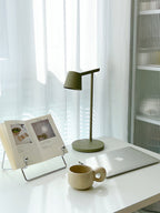 Olive Clérachic table lamp on a white desk beside a laptop, a book stand and a small cream cup.