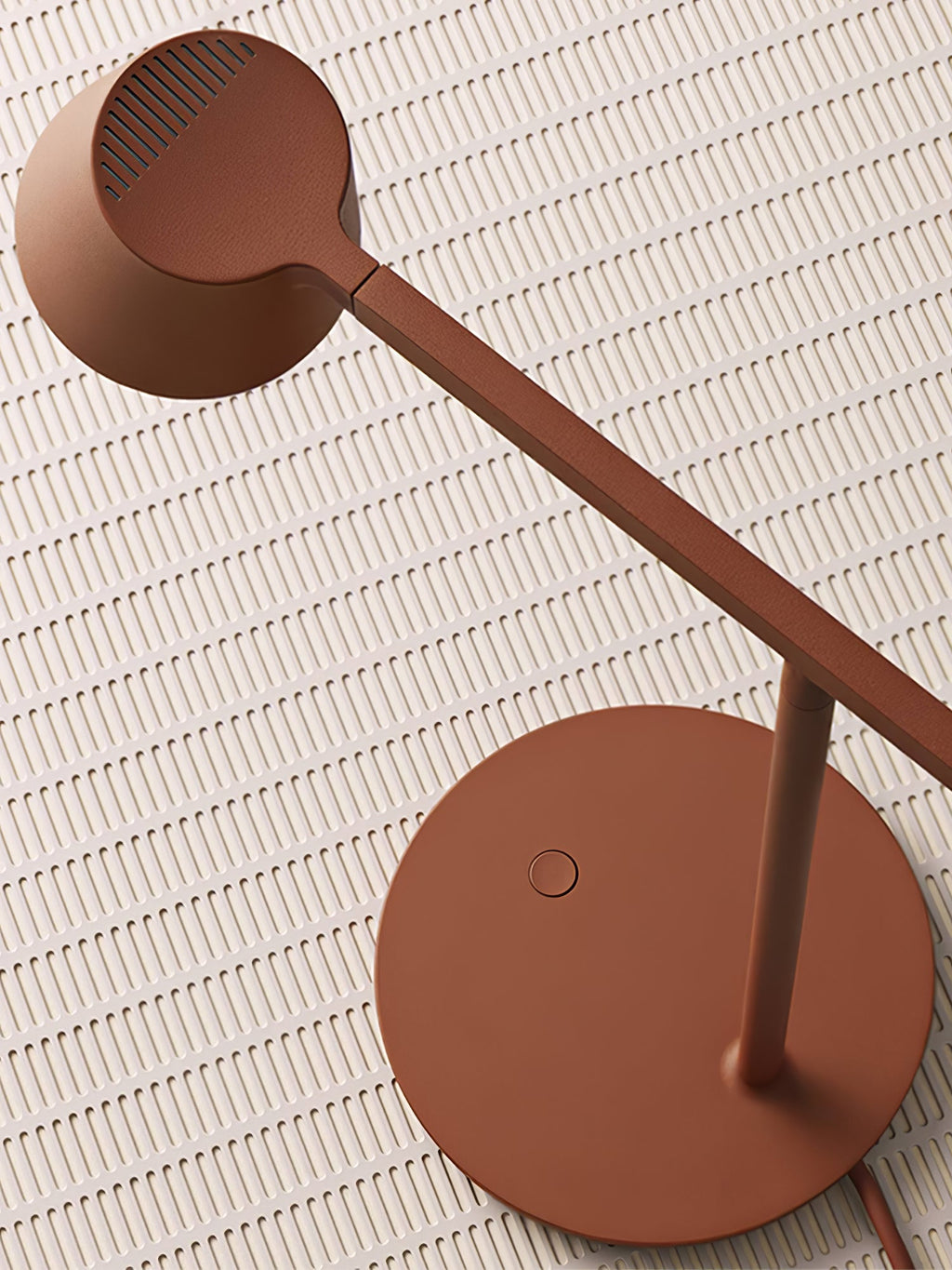 Overhead close view of a rust-red Clérachic table lamp, with its round head and base on a ribbed pale tile.