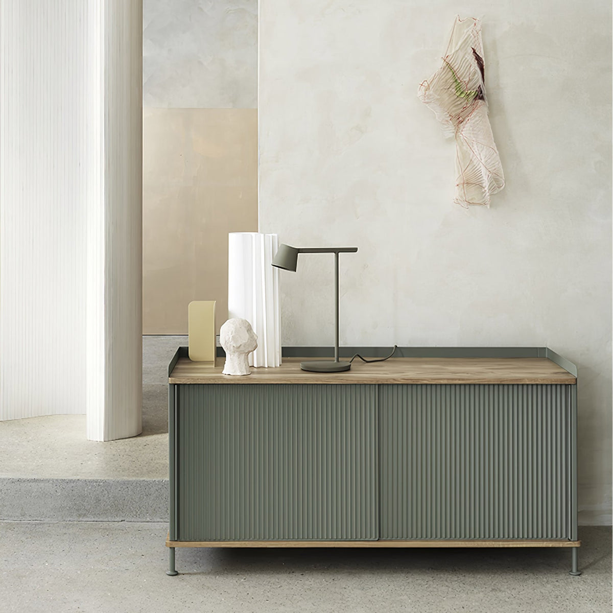 Olive Clérachic table lamp on a green ribbed sideboard in a plaster-toned room, with white vases beside it.