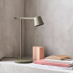 This Clérachic table lamp in olive on a concrete ledge, with a pink block and a few stacked books.