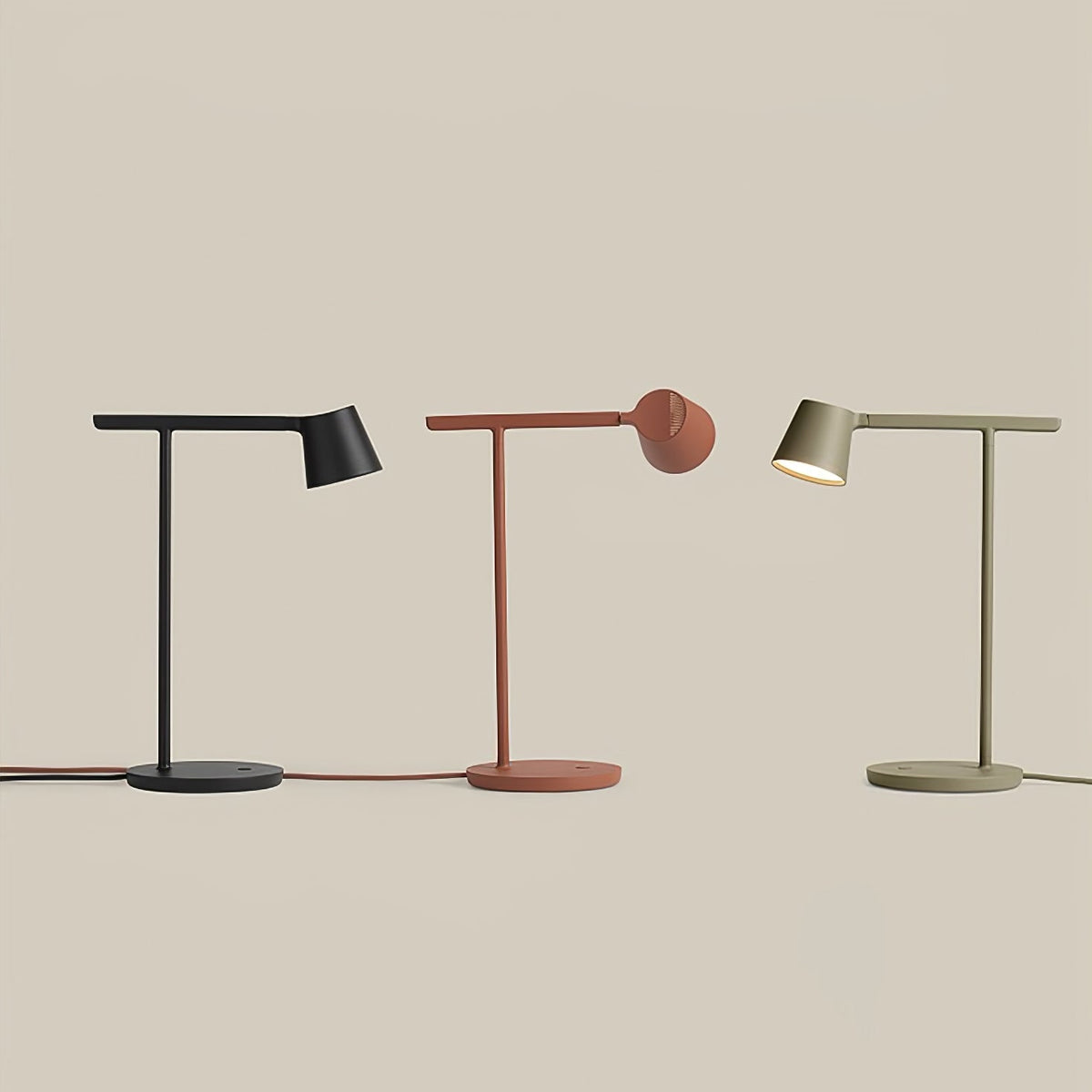 A trio of Clérachic table lamps in black, rust-red and olive standing in a row on a beige backdrop.