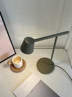 A dark-green version of this Clérachic table lamp lit above a white desk, with a candle in a cup and a notebook.