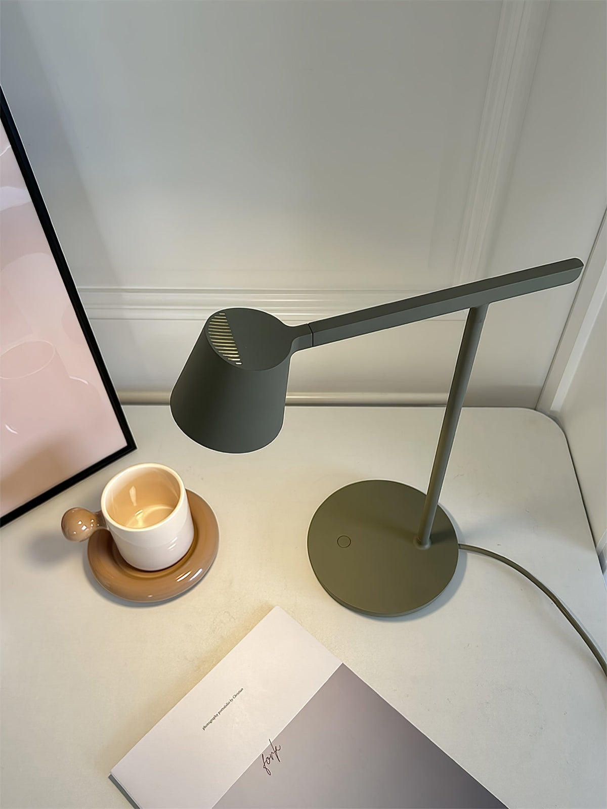 A dark-green version of this Clérachic table lamp lit above a white desk, with a candle in a cup and a notebook.