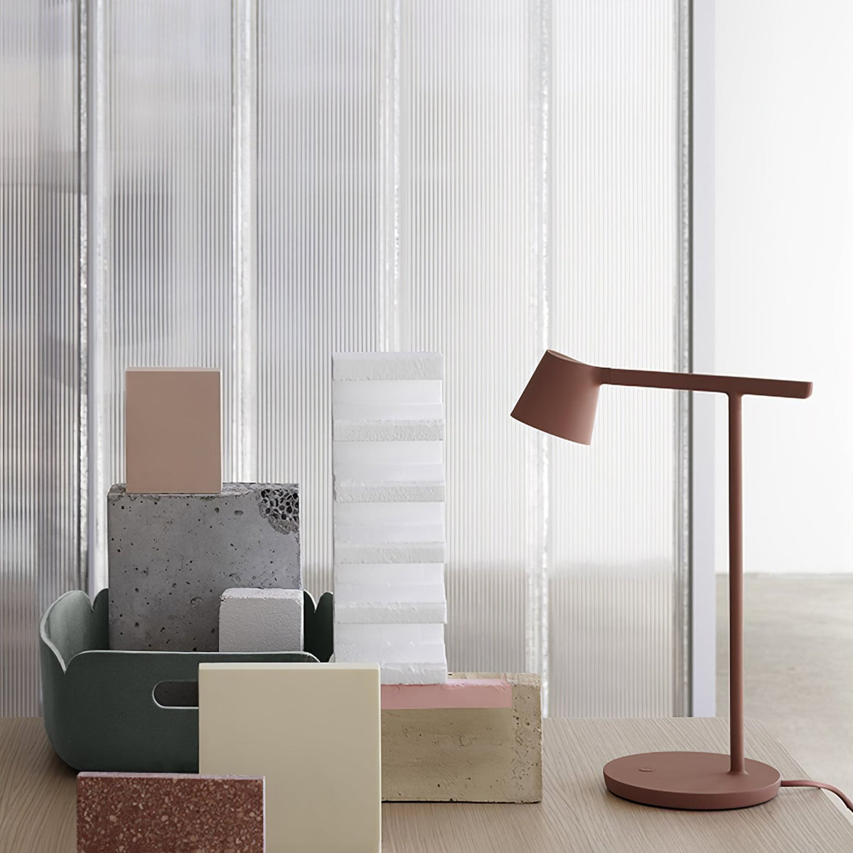 A rust-red Clérachic table lamp in a stack of pastel blocks, against a ribbed glass backdrop.