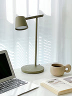 This Clérachic table lamp in olive switched on beside a laptop, a stoneware cup and an open book.