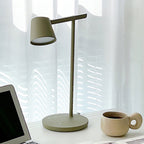 Close view of the olive head of a Clérachic table lamp, lit on the underside, with a laptop and a mug at the edges.