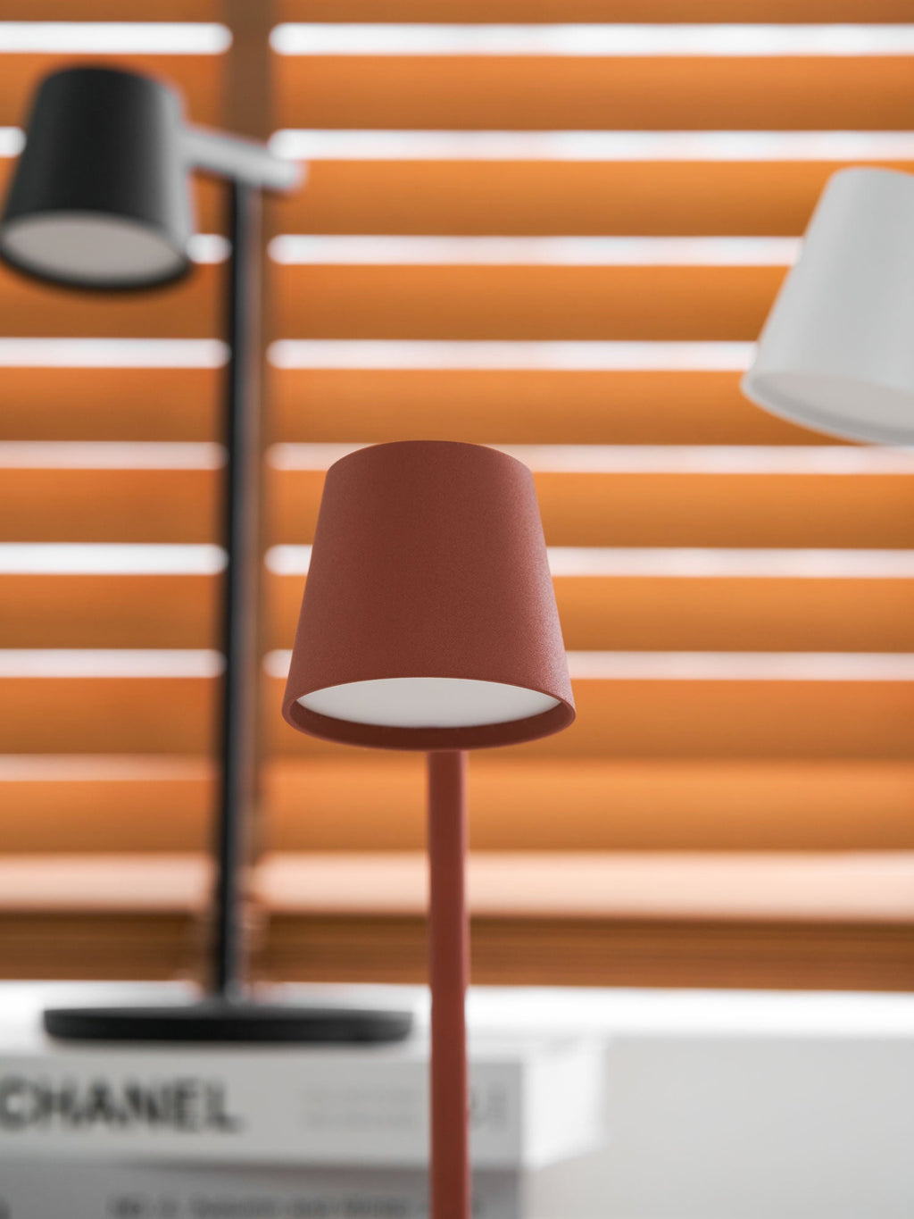 Close view of the red lamp head from this Clérachic table lamp, with the black and white lamps softly blurred behind.