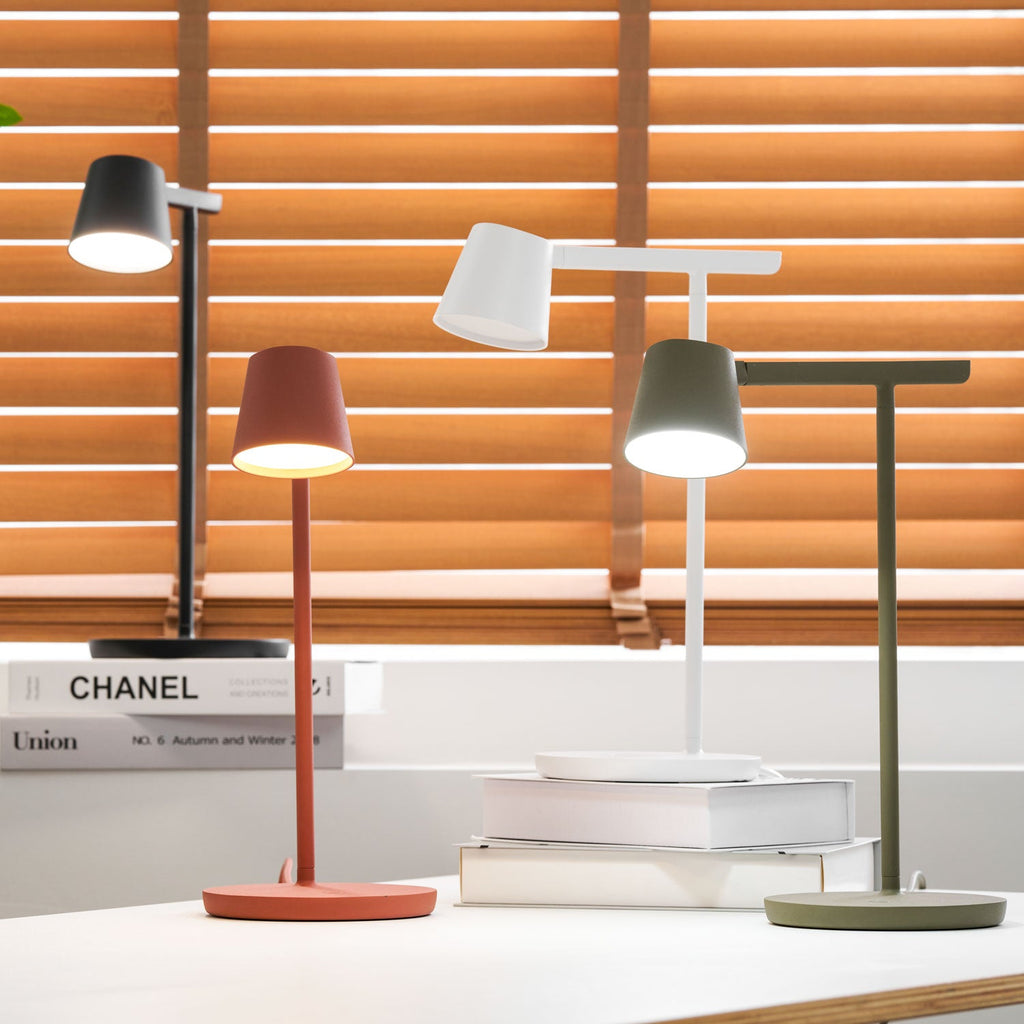 A Clérachic table lamp group with the red and olive heads switched on, set against orange blinds.