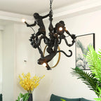 This Clérachic monkey chandelier in black, hung in a bright room with a gold-framed round mirror and green palm leaves behind.