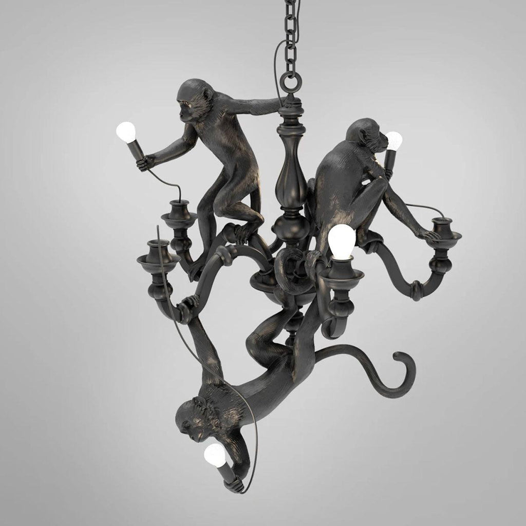 Black Clérachic chandelier with its three resin monkeys, one hanging by its tail with a bulb, on a plain grey background.