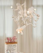 A Clérachic white monkey chandelier lit before sheer cream curtains, with a bag of pink flowers on a table beneath it.