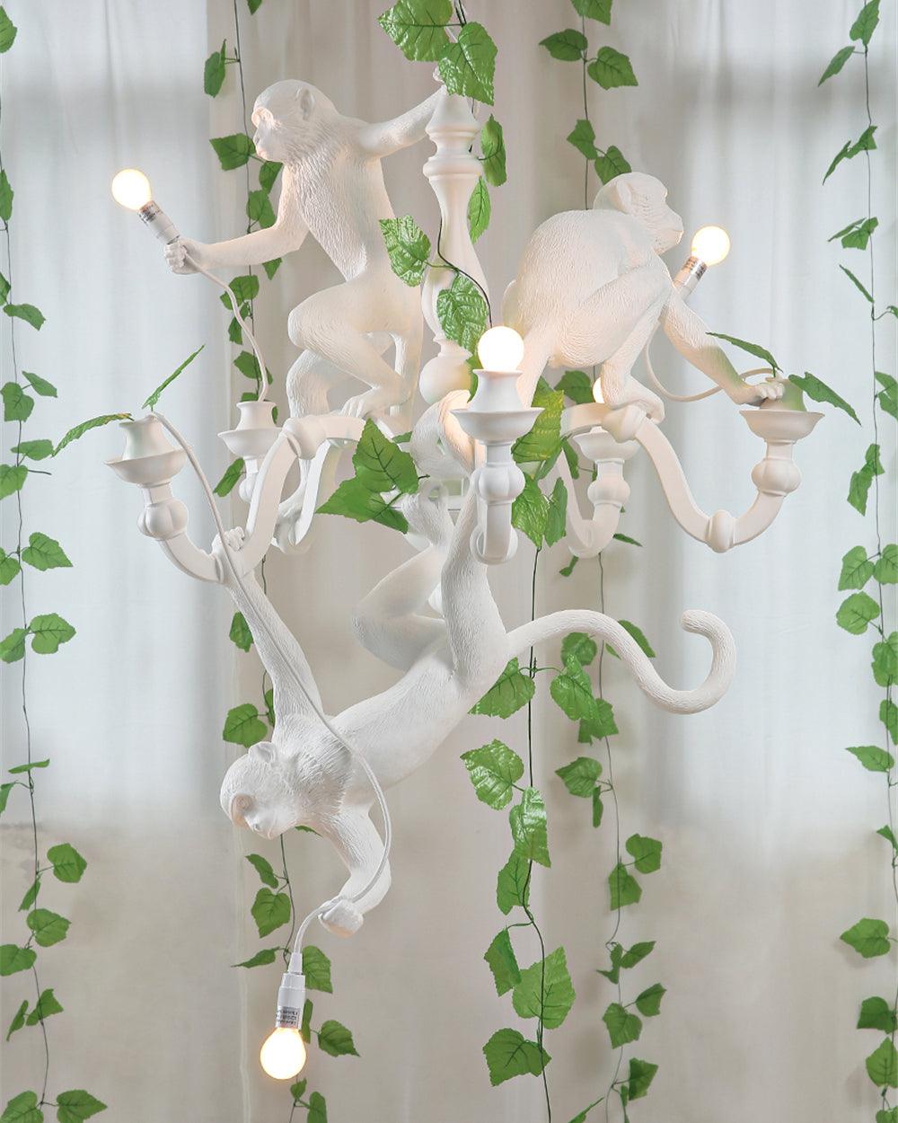 White Clérachic monkey chandelier lit among trailing green ivy in front of sheer curtains, bulbs shining from its candle-style arms.