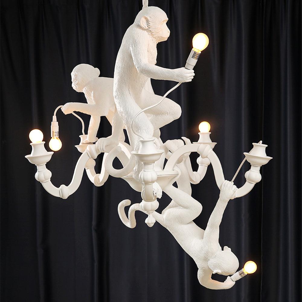 Close view of the three white monkeys on this Clérachic chandelier, each holding a lit bulb, against a dark navy curtain.
