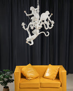 Clérachic white monkey chandelier hung high in front of dark curtains, above a mustard-yellow sofa and a potted plant.