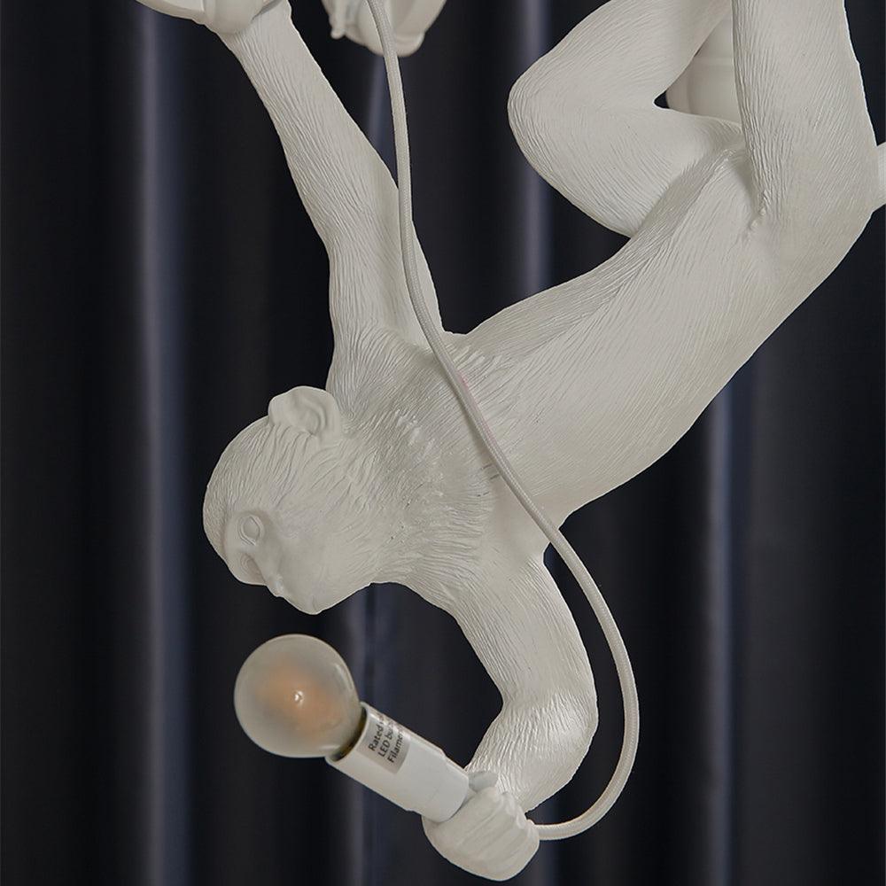 Close view of the monkey hanging upside down with a bulb in its hand on this Clérachic chandelier, with a white cable trailing behind.