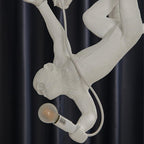 Close view of the monkey hanging upside down with a bulb in its hand on this Clérachic chandelier, with a white cable trailing behind.