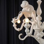 Close view of a white monkey perched on a candle-style arm holding a lit bulb, on this Clérachic chandelier.