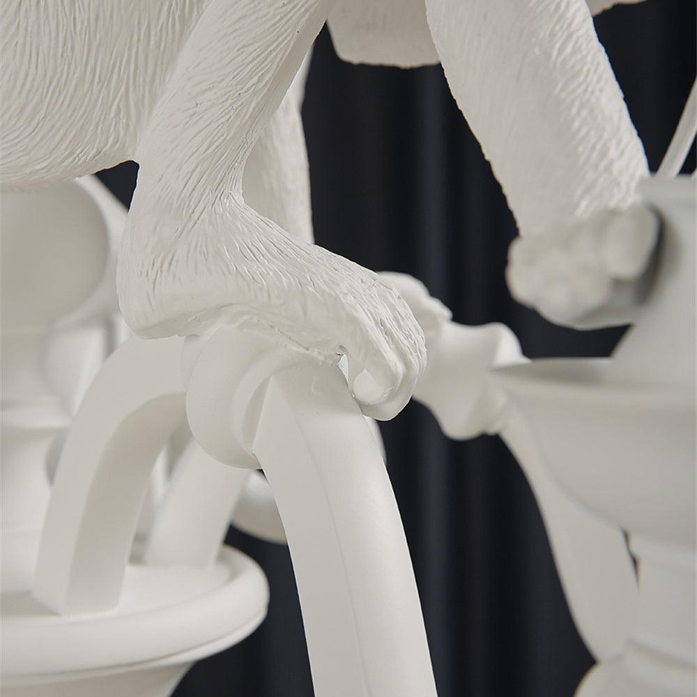 Close view of a monkey's hand and arm gripping a curved arm of this white Clérachic chandelier, with the textured resin visible.